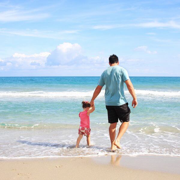 man holding childs hand at the beach